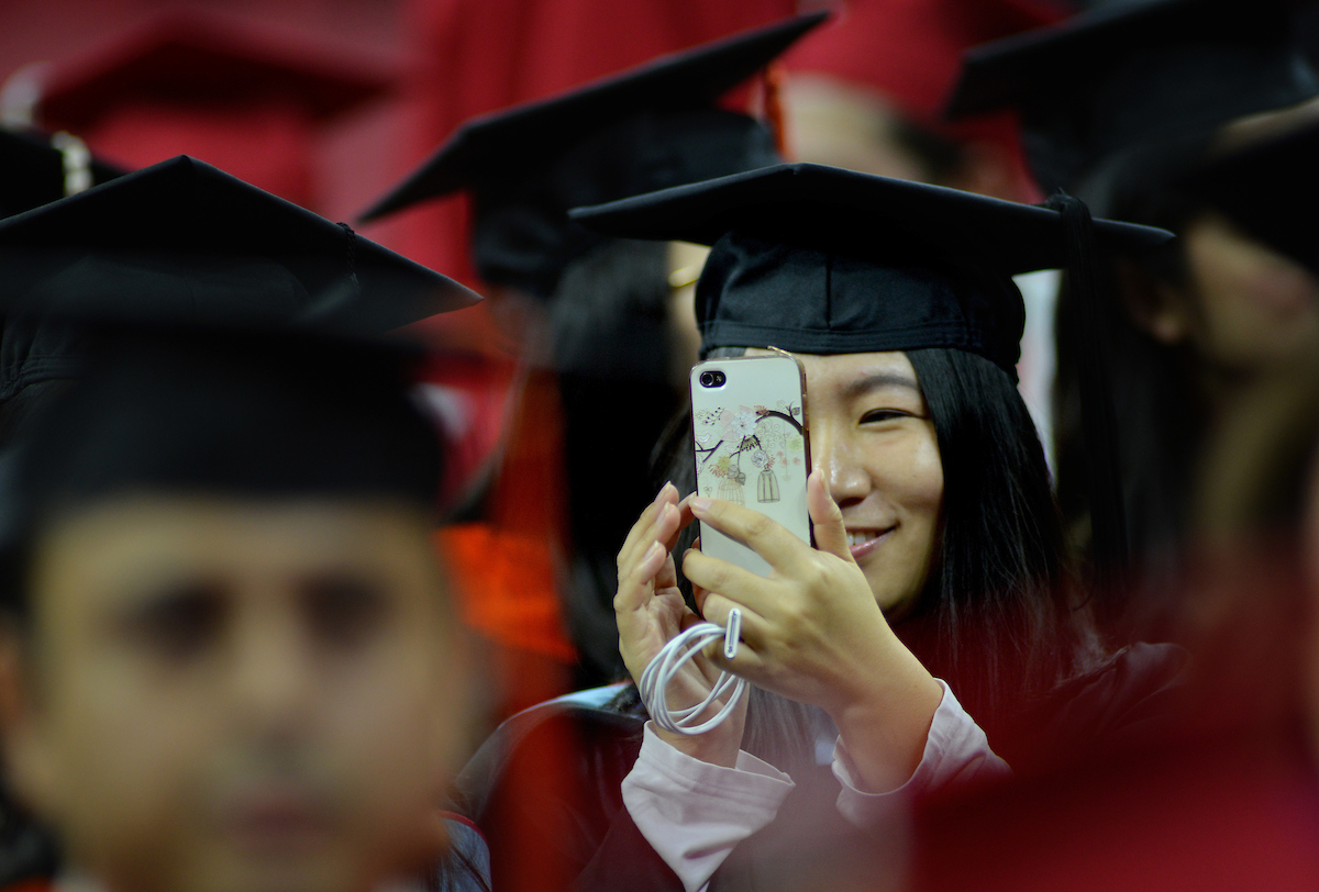 Graduate student documents commencement with her phone.
